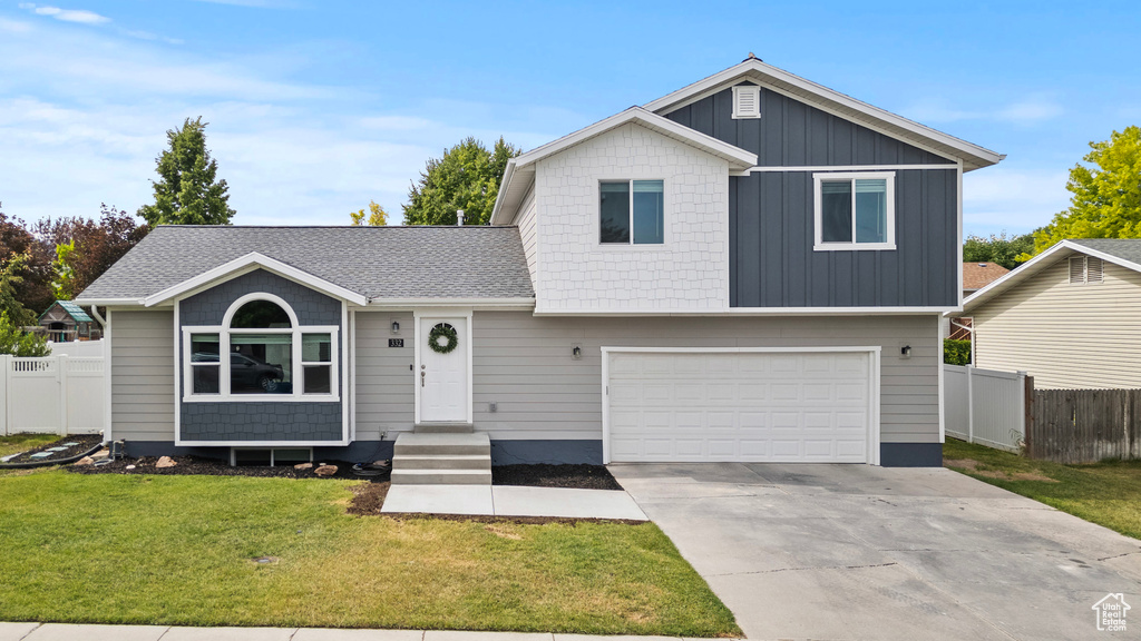 Tri-level home featuring a garage, board and batten siding, driveway, and roof with shingles