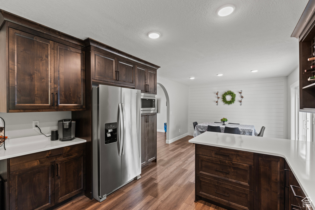Kitchen with stainless steel appliances, arched walkways, dark wood finished floors, dark brown cabinets, and light countertops