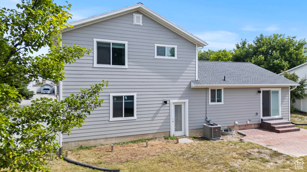 Rear view of house with entry steps, a patio, roof with shingles, and a yard