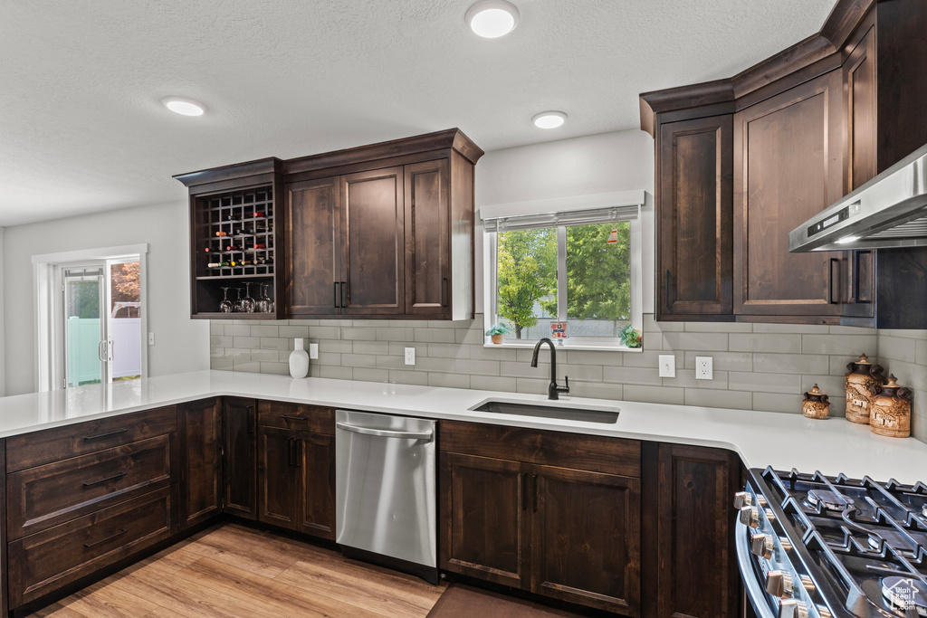 Kitchen featuring dishwasher, wall chimney exhaust hood, light countertops, light wood finished floors, and dark brown cabinets