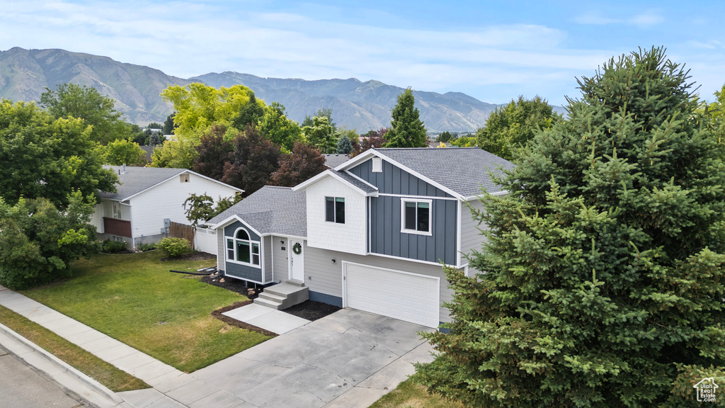 View of front facade with board and batten siding, a garage, concrete driveway, a mountain view, and a front yard