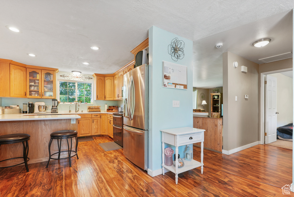 Kitchen featuring appliances with stainless steel finishes, wood finished floors, light countertops, glass insert cabinets, and a kitchen bar