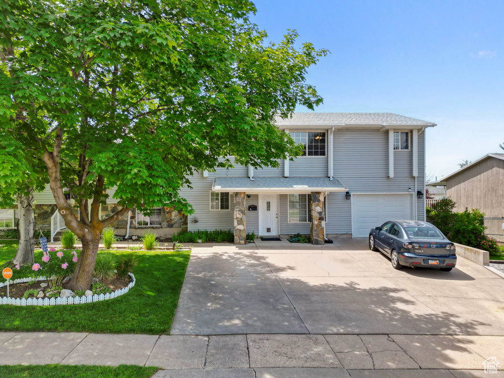 View of front of property featuring concrete driveway, a garage, stone siding, and a front yard