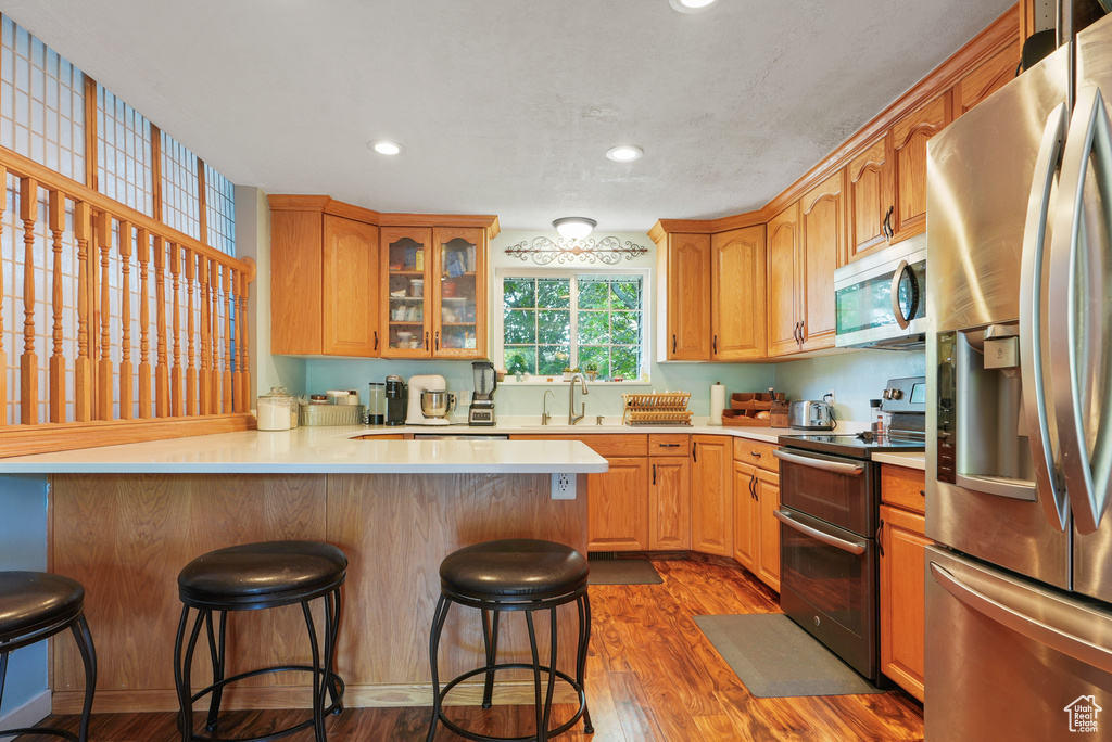 Kitchen with stainless steel appliances, a peninsula, a kitchen bar, light countertops, and recessed lighting