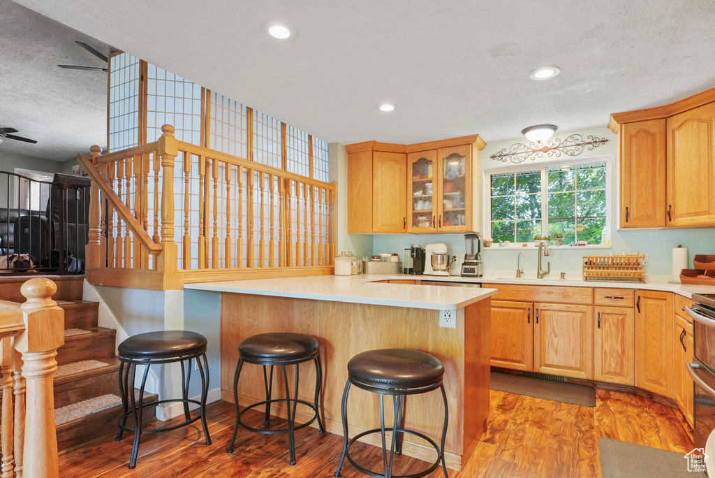 Kitchen featuring a kitchen breakfast bar, light wood finished floors, glass insert cabinets, light countertops, and recessed lighting