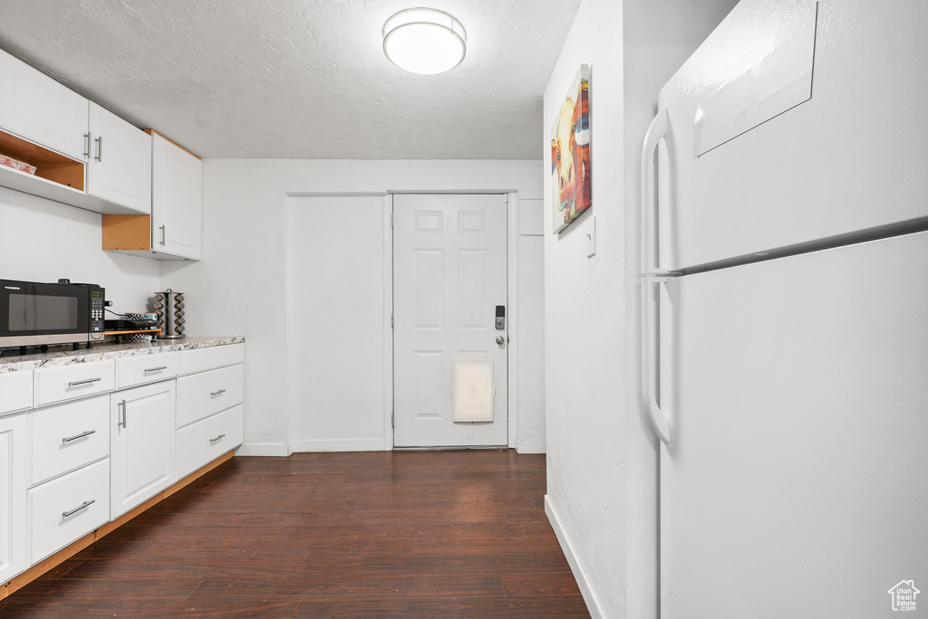 Kitchen with freestanding refrigerator, black microwave, dark wood-style flooring, white cabinetry, and light stone counters