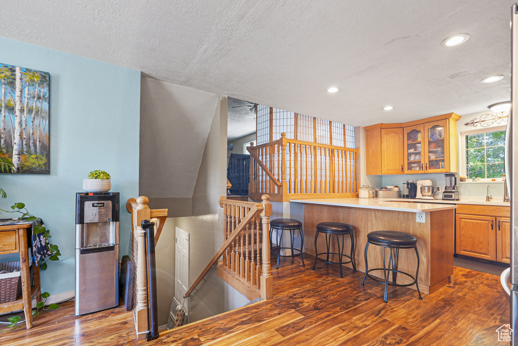 Kitchen with wood finished floors, a textured ceiling, a kitchen bar, glass insert cabinets, and light countertops