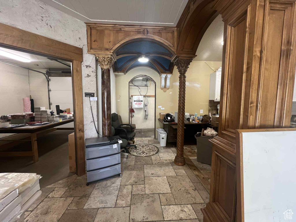 Hallway featuring decorative columns, stone tile flooring, and arched walkways