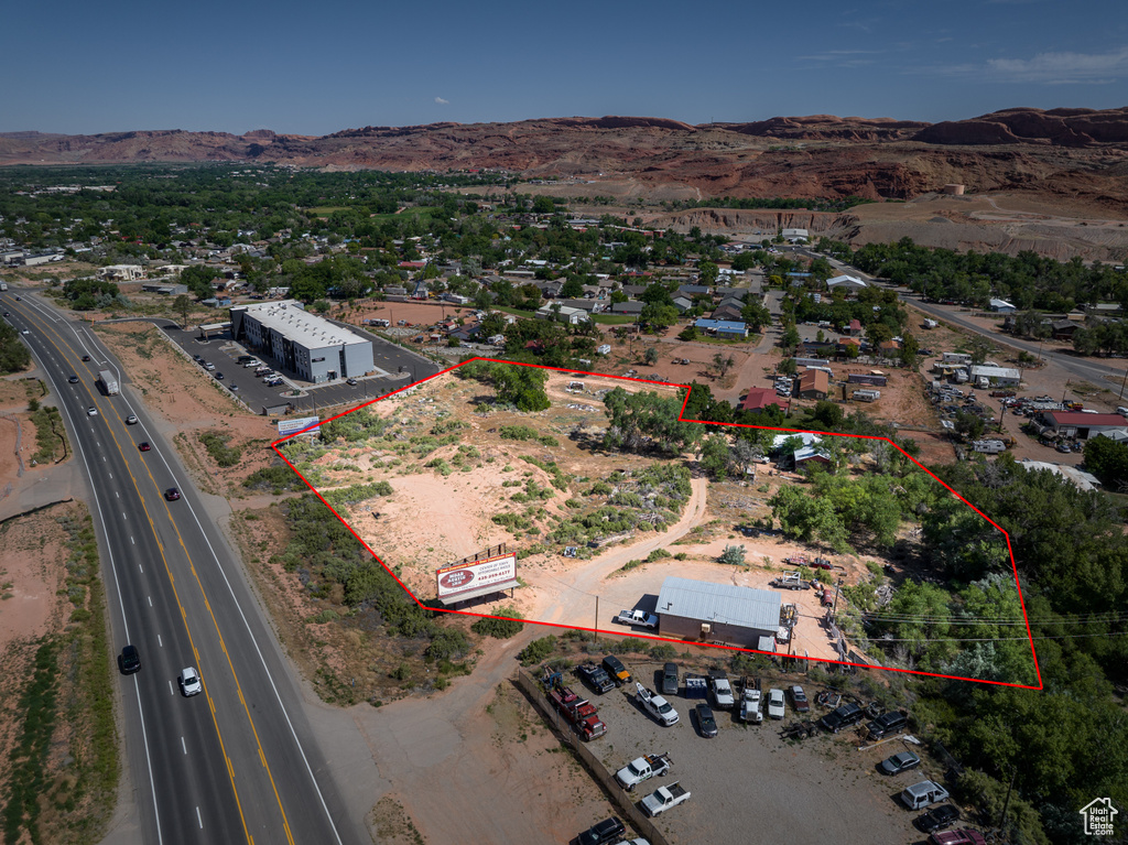 Aerial view of property and surrounding area featuring property boundaries highlighted, a mountainous background, and a main thoroughfare