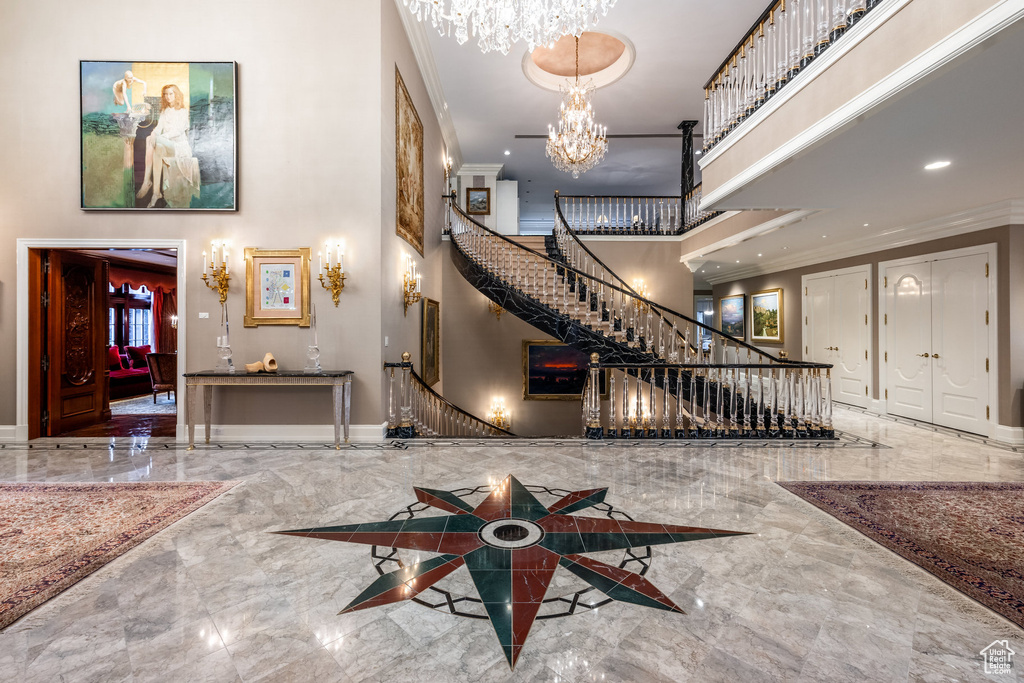 Foyer entrance featuring a high ceiling, marble tiled flooring, a chandelier, ornamental molding, and stairs