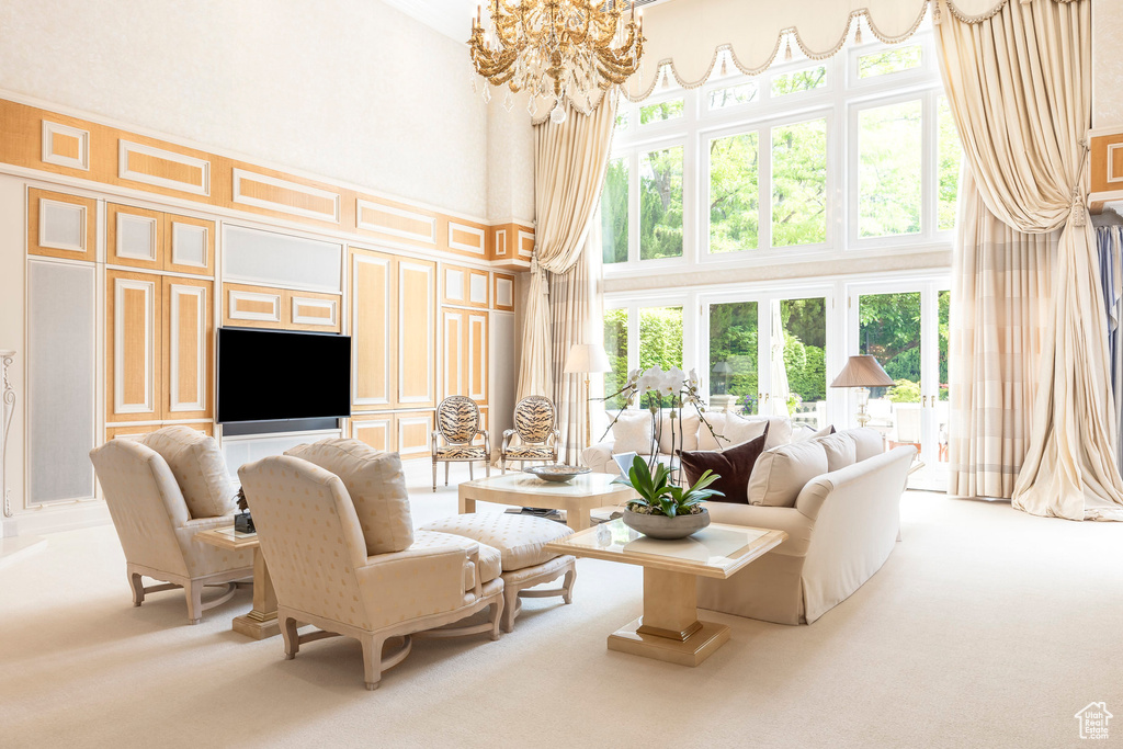 Carpeted living area with a high ceiling, plenty of natural light, a chandelier, and a decorative wall