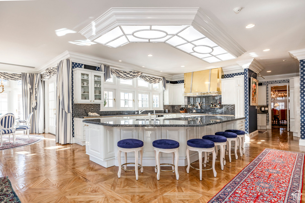 Kitchen with custom exhaust hood, crown molding, a kitchen bar, decorative backsplash, and glass insert cabinets