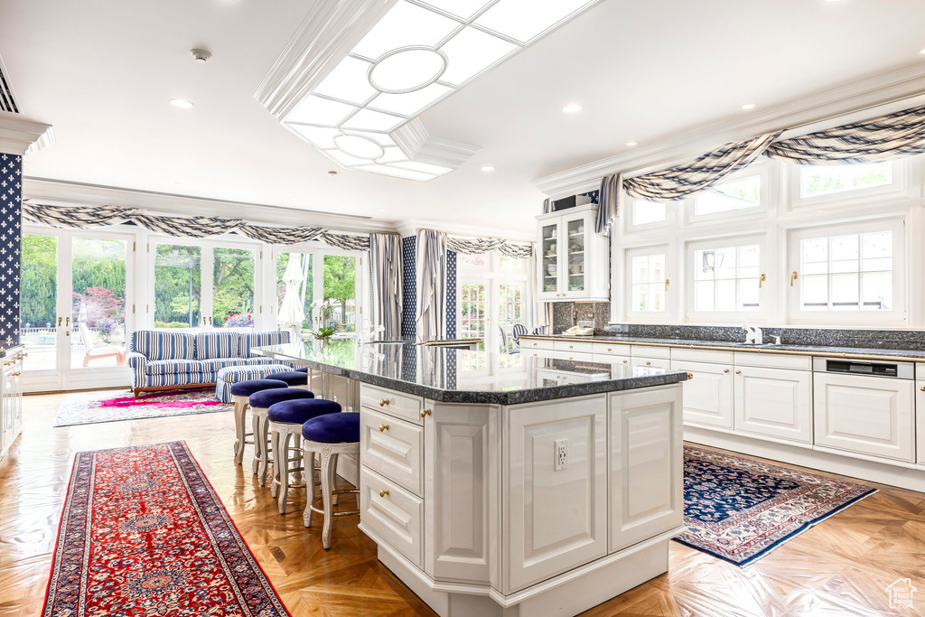 Kitchen with crown molding, a center island, a breakfast bar, white cabinets, and glass insert cabinets