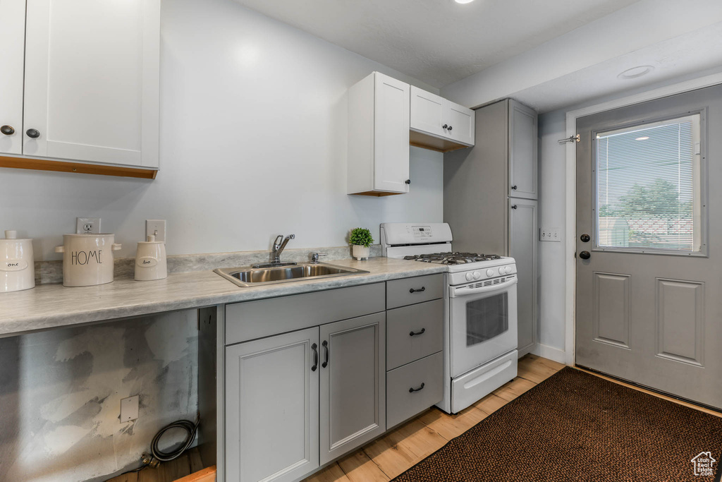 Kitchen with white gas range, gray cabinetry, light wood finished floors, and light countertops