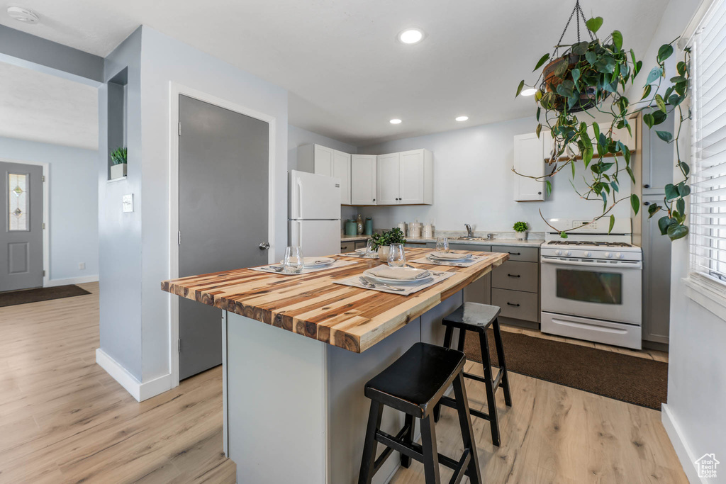 Kitchen featuring white appliances, wooden counters, a kitchen breakfast bar, light wood-type flooring, and recessed lighting