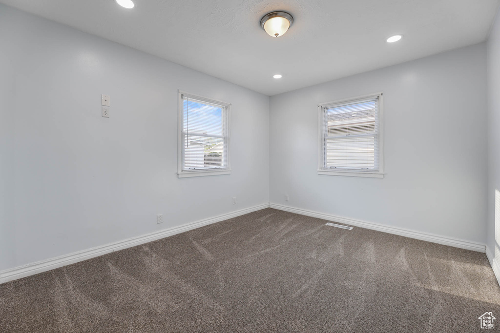 Unfurnished room featuring dark colored carpet, healthy amount of natural light, and recessed lighting