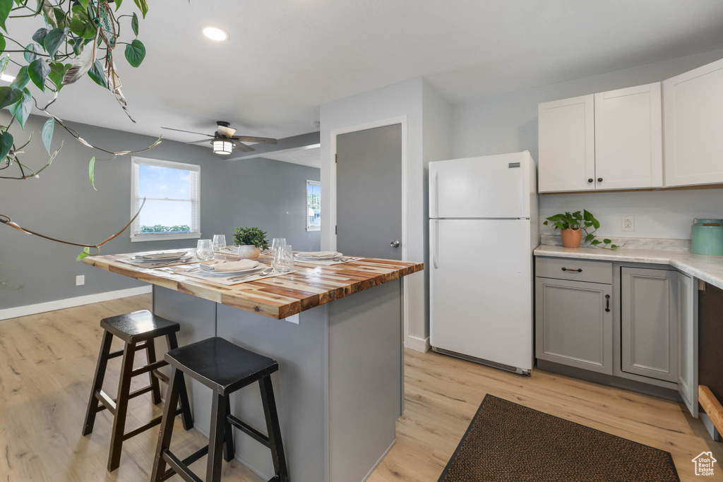 Kitchen with freestanding refrigerator, butcher block counters, light wood-style flooring, and a kitchen bar