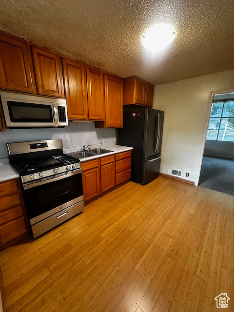 Kitchen with appliances with stainless steel finishes, brown cabinetry, light countertops, light wood-type flooring, and a textured ceiling