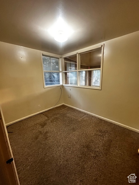 Unfurnished room featuring dark carpet and baseboards