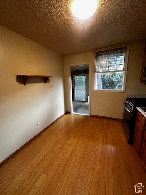 Kitchen featuring range with gas stovetop, light wood finished floors, a textured ceiling, and stainless steel microwave