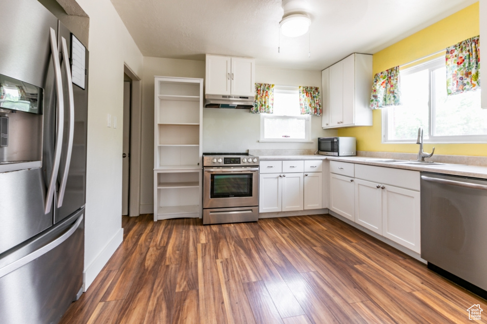 Kitchen with appliances with stainless steel finishes, under cabinet range hood, healthy amount of natural light, and white cabinets