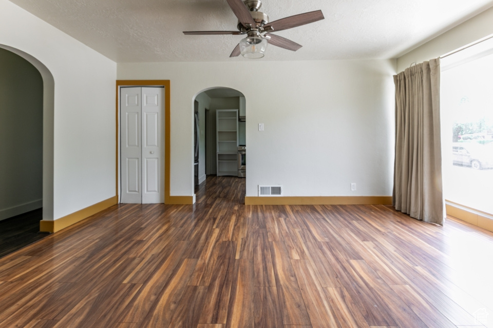 Empty room featuring ceiling fan, arched walkways, dark wood-style flooring, and a textured ceiling