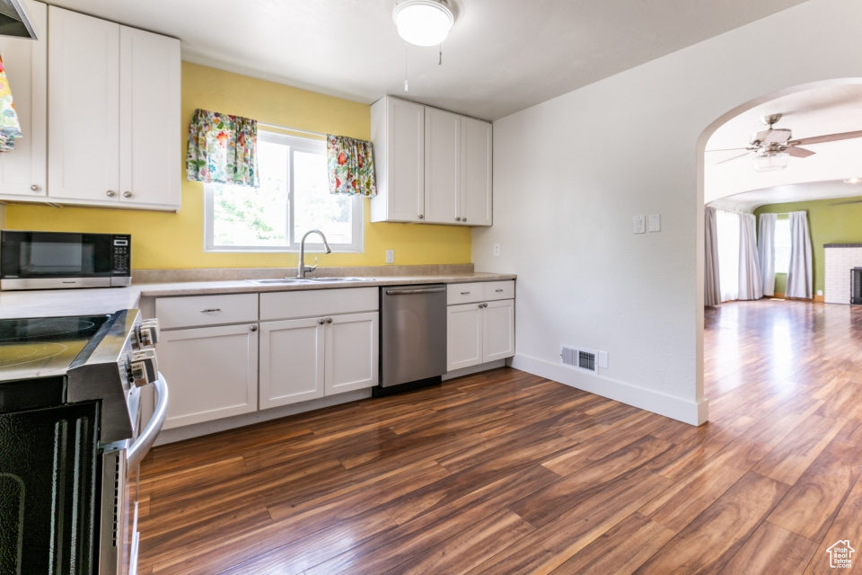 Kitchen featuring stainless steel appliances, ceiling fan, dark wood-style floors, and arched walkways