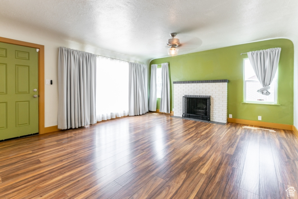 Unfurnished living room featuring a ceiling fan, wood finished floors, and a fireplace