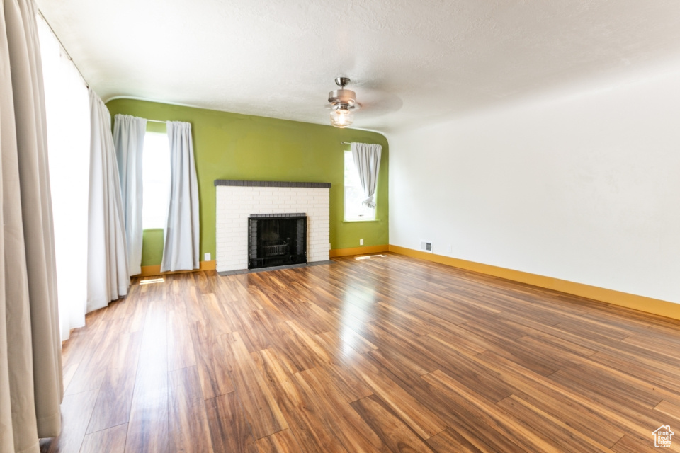 Unfurnished living room featuring healthy amount of natural light, ceiling fan, wood finished floors, and a fireplace