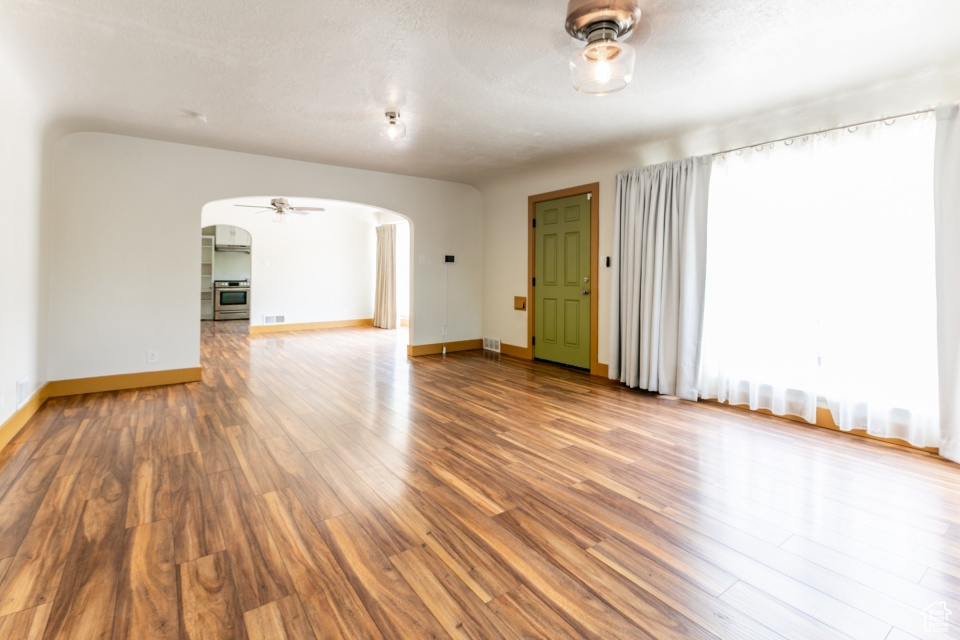 Unfurnished living room featuring arched walkways, ceiling fan, and wood finished floors