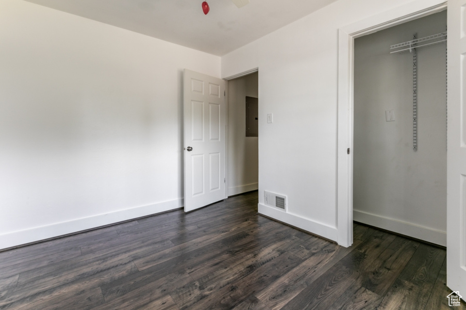 Unfurnished bedroom with electric panel, dark wood finished floors, and a closet