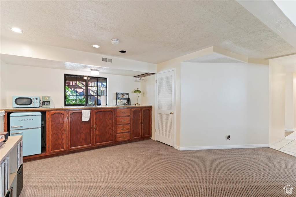 Kitchen featuring light carpet, white microwave, a textured ceiling, light countertops, and recessed lighting