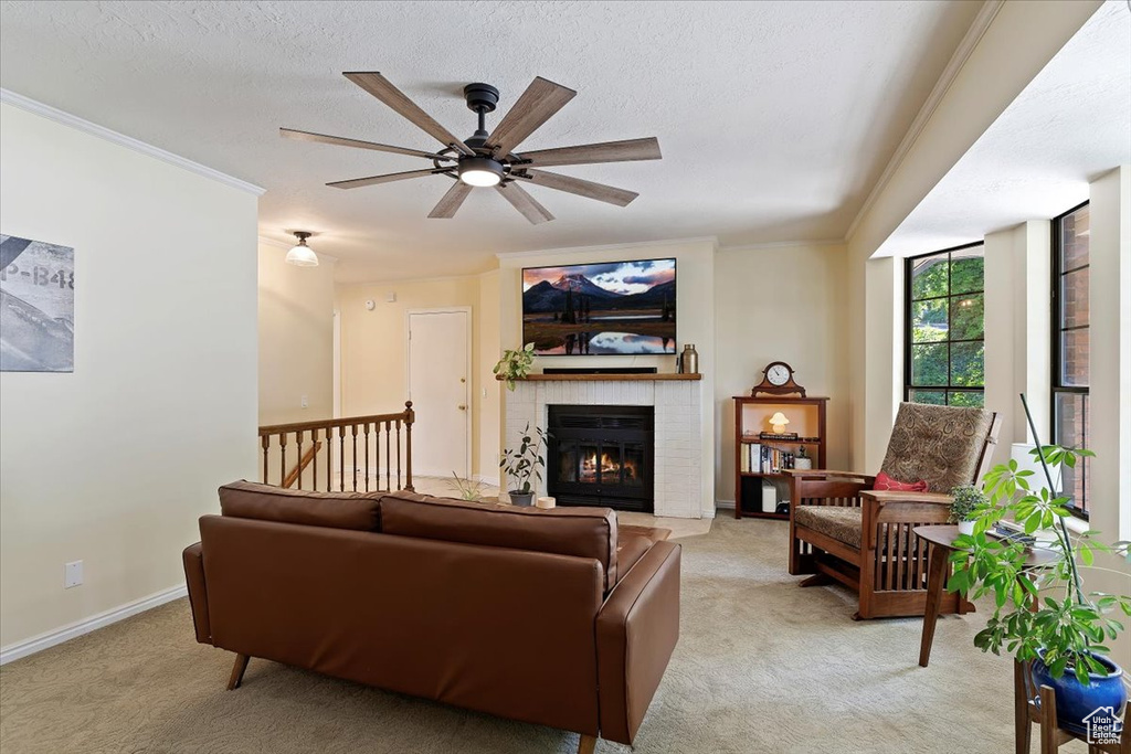 Living area featuring light colored carpet, ceiling fan, a fireplace, ornamental molding, and a textured ceiling
