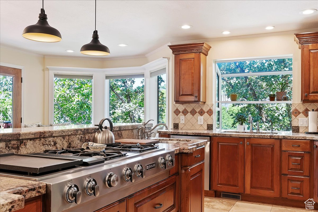 Kitchen with stainless steel gas cooktop, light stone countertops, hanging light fixtures, backsplash, and brown cabinetry