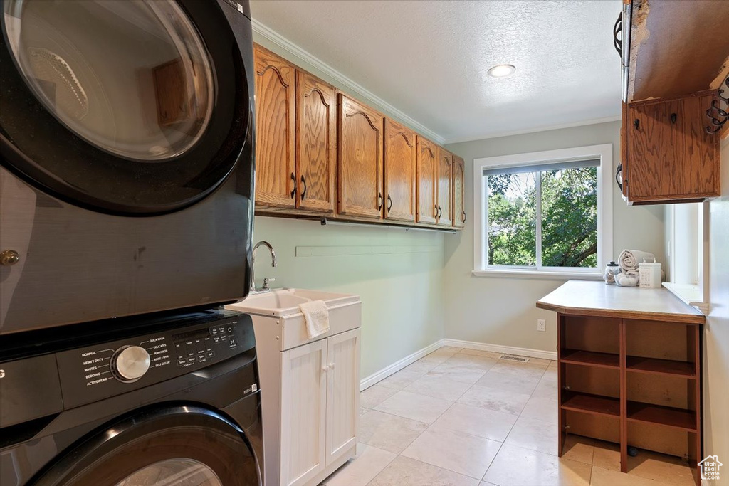 Washroom featuring stacked washer / dryer, cabinet space, a textured ceiling, and light tile patterned floors