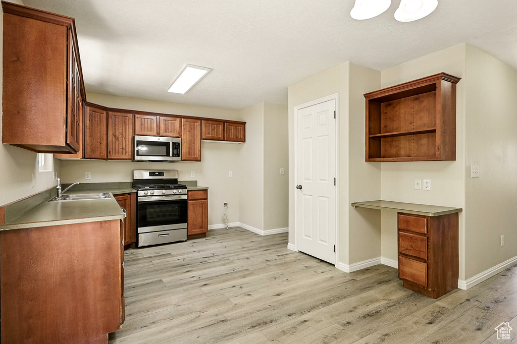 Kitchen featuring appliances with stainless steel finishes, light wood finished floors, built in study area, brown cabinetry, and open shelves