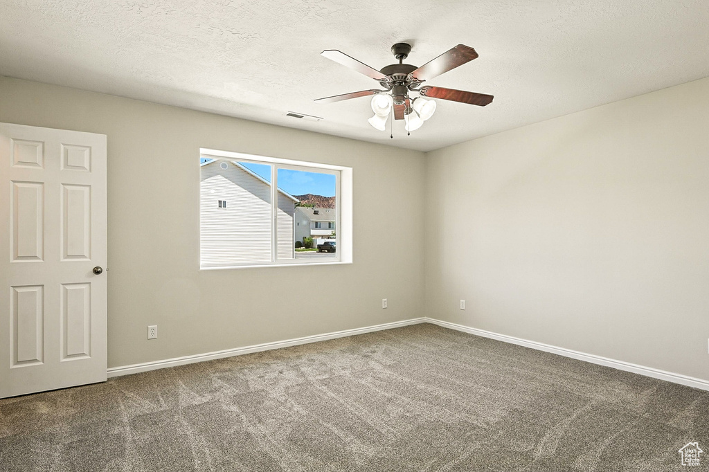 Carpeted empty room with ceiling fan and a textured ceiling