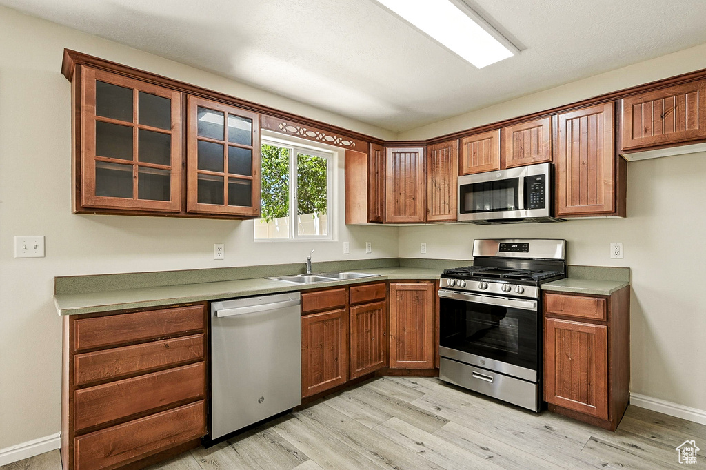 Kitchen featuring stainless steel appliances, light wood finished floors, glass insert cabinets, and brown cabinets