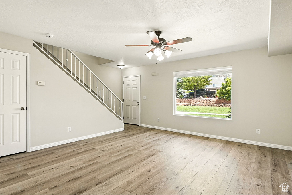 Unfurnished living room with a ceiling fan, light wood finished floors, and stairway