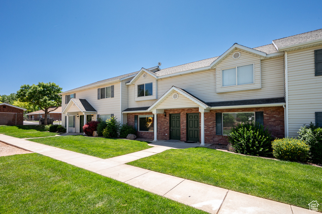 Townhome / multi-family property with a front lawn, brick siding, and a shingled roof