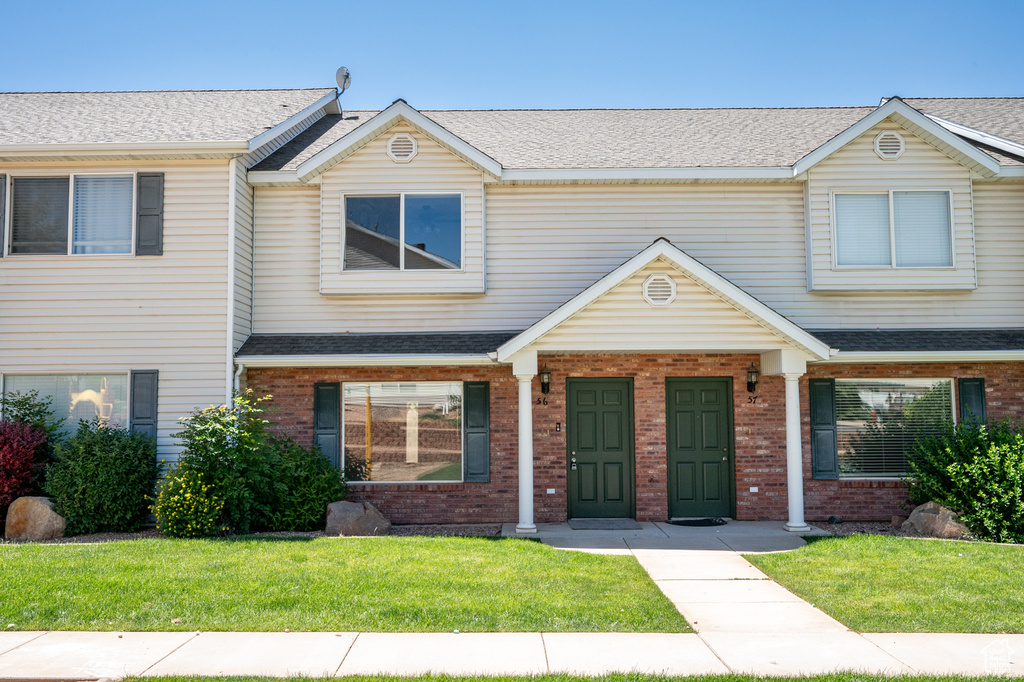 Townhome / multi-family property featuring brick siding, a front yard, and roof with shingles