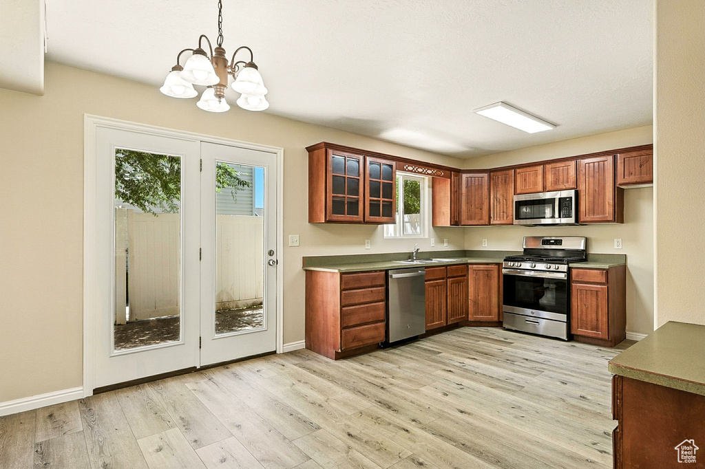 Kitchen featuring appliances with stainless steel finishes, light wood-style flooring, a chandelier, glass insert cabinets, and decorative light fixtures