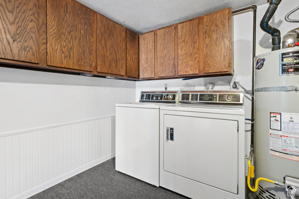 Washroom featuring secured water heater, separate washer and dryer, cabinet space, dark colored carpet, and a wainscoted wall