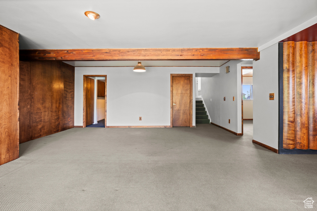 Carpeted spare room with beamed ceiling and stairway