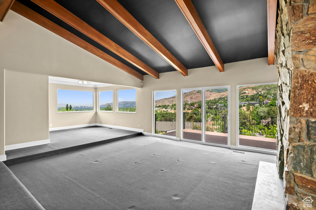 Unfurnished living room with beam ceiling, plenty of natural light, carpet flooring, and high vaulted ceiling