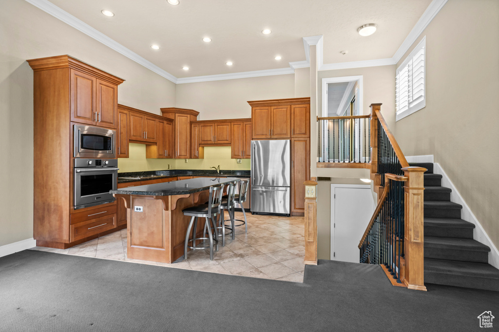 Kitchen featuring stainless steel appliances, a kitchen bar, a kitchen island, crown molding, and a towering ceiling