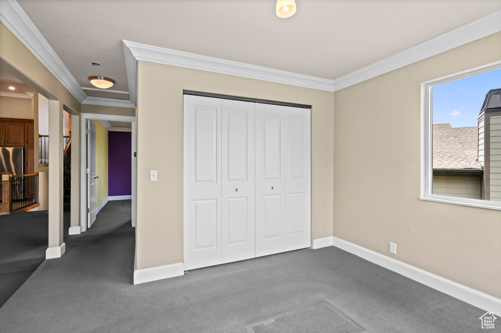 Unfurnished bedroom with crown molding, dark colored carpet, and a closet