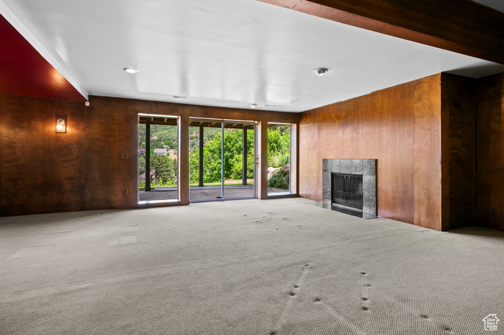 Unfurnished living room featuring wooden walls, carpet, and a fireplace