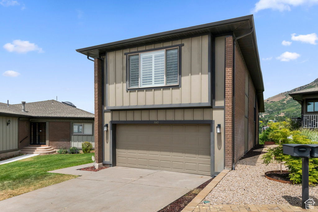 View of front of house featuring board and batten siding, an attached garage, concrete driveway, brick siding, and a front yard