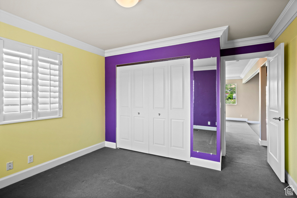 Unfurnished bedroom featuring ornamental molding, a closet, and dark colored carpet